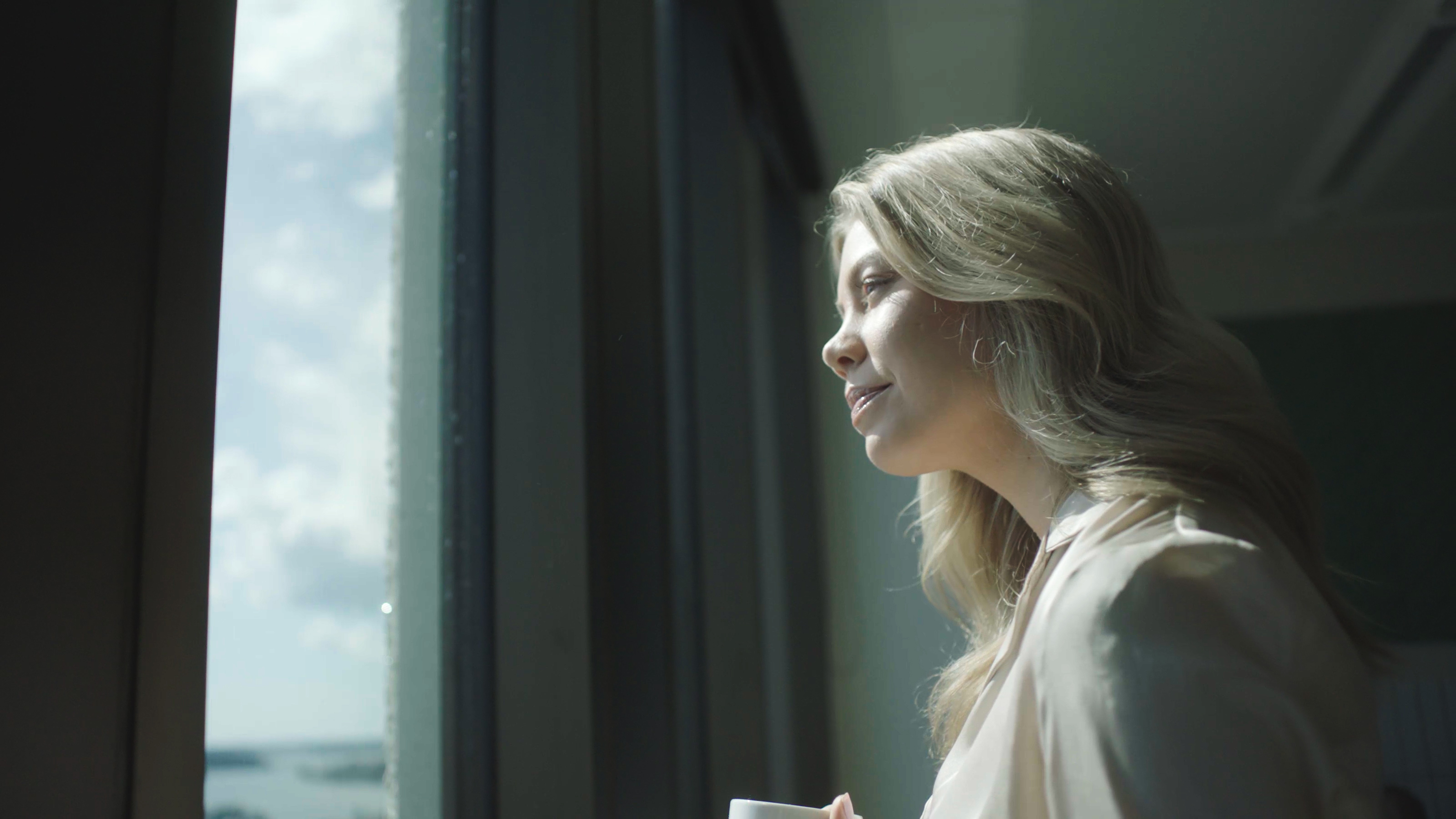 nainen katsoo maisemaa ikkunasta