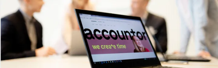 En pc i et rom med masse mennesker, pcen står i fokus med teksten "we create time" på skjermen 