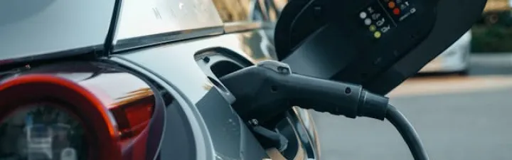 En sølvfarget elbil med ladekabelen plugget i. Man ser den bakfra med ene lykten. 